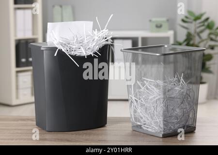 Distruggendo fogli con trituratore e strisce di carta in un cestino di metallo su un tavolo di legno in ufficio Foto Stock