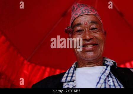 Bhaktapur, Nepal. 31 agosto 2024. Un devoto sorride mentre tiene in mano un ombrello tradizionale per le persone nascoste all'interno dell'idolo della divinità Dipankar Buddha mentre sfilano per l'antica città per ricevere le preghiere offerte dai devoti durante il festival Pancha Dan in Bhaktapur Durbar Square. Le principali attrazioni del festival sono la donazione di cinque elementi, noti anche come cinque regali estivi, tra cui grani di grano, grani di riso, sale, denaro e frutta per le preghiere, augurando buona salute e prosperità. I buddisti osservano Pancha Dan mostrando gigantesche statue antiche di Deity Dipankar Buddha e devoto Foto Stock