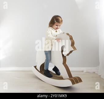 Adorabili toddler sorridente ragazza seduta sul cavallo a dondolo Foto Stock