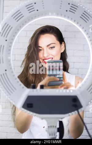 Giovane e bella donna prendendo selfie foto con il telefono cellulare nella luce della lampada ad anello Foto Stock