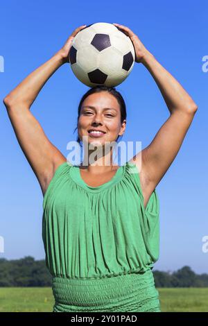 Giovane donna colombiana che tiene il calcio in testa nel cielo blu Foto Stock