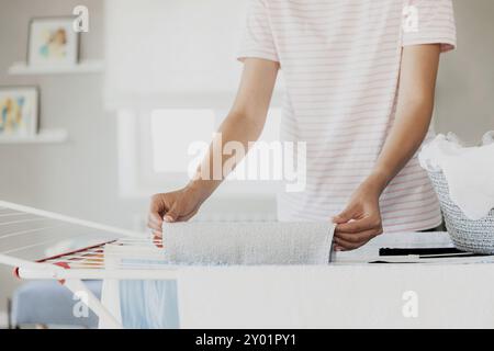 Donna appeso pulito bagnato vestiti lavanderia su scaffale di asciugatura a casa in camera. Particolare della donna casalinga mani closeup appeso lavanderia su abbigliamento rack dye Foto Stock