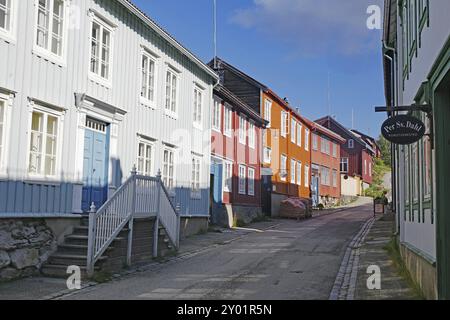 Una strada tranquilla con tradizionali case in legno in diversi colori sotto un cielo soleggiato, patrimonio dell'umanità dell'UNESCO, città dei minatori, Roeros, Norvegia, Europa Foto Stock