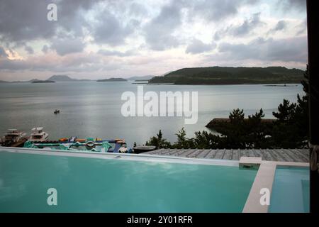 Dolsan-eup, Yeosu-si, Corea del Sud - 26 luglio 2024: Giovane donna che guarda l'alba in un resort con piscina affacciata sul mare di Yeosu Foto Stock