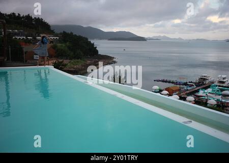 Dolsan-eup, Yeosu-si, Corea del Sud - 26 luglio 2024: Giovane donna che guarda l'alba in un resort con piscina affacciata sul mare di Yeosu Foto Stock