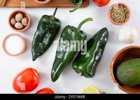 Una vista dall'alto verso il basso di tre peperoncini poblano, tra gli altri ingredienti della salsa. Foto Stock