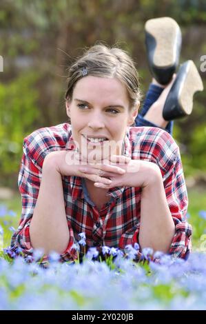 Bella giovane donna sdraiata in un prato con un blueterchen in fiore (scilla bifolia) in primavera e si gode la calda luce del sole giovane attraente donna Foto Stock