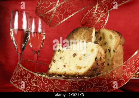 Panettone la torta di frutta natalizia italiana servita su un piatto di vetro rosso su sfondo rosso con decorazioni a stella dorata, nastro e due bicchieri di c Foto Stock