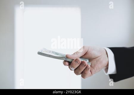 Un pacchetto di banconote da cento dollari, in mano a un uomo in tuta e camicia bianca. Sfondo sfocato. Foto Stock