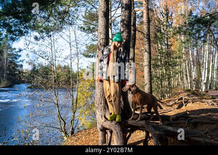 Una donna appassionata di cani ama passeggiare con il suo animale domestico vizsla nella foresta vicino al fiume ghiacciato alla fine del giorno autunnale. Foto Stock