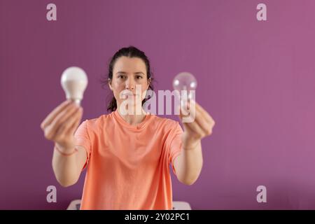 Confronto tra lampadine economiche e normali. Concetto di vita ecologica e sostenibilità - donna sorridente che confronta la lampadina a risparmio energetico con quella a incandescenza Foto Stock