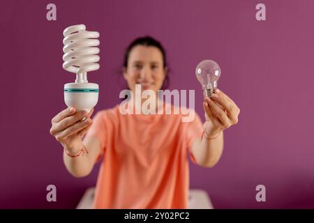 Confronto tra lampadine economiche e normali. Concetto di vita ecologica e sostenibilità - donna sorridente che confronta la lampadina a risparmio energetico con quella a incandescenza Foto Stock