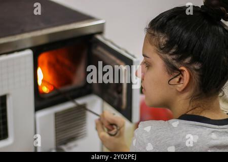 Povera ragazza che mette legna da ardere nella stufa in casa, concetto di povertà. Foto Stock