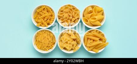 Ciotole con diversi tipi di pasta su sfondo azzurro, vista dall'alto Foto Stock