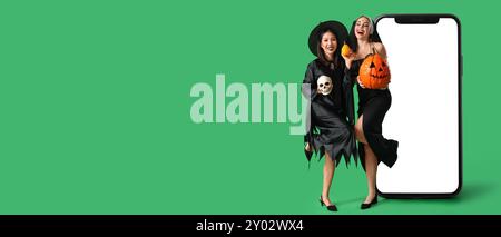 Donne felici con costumi di Halloween e grande smartphone su sfondo verde con spazio per il testo Foto Stock