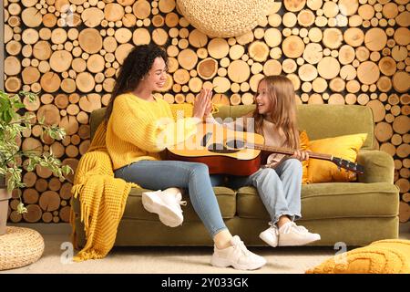 Giovane donna e ragazza con chitarra acustica che si danno a vicenda cinque alti a casa Foto Stock