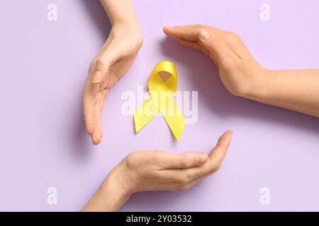 Mani da donna e nastro giallo su sfondo lilla. Concetto di sarcoma. Foto Stock