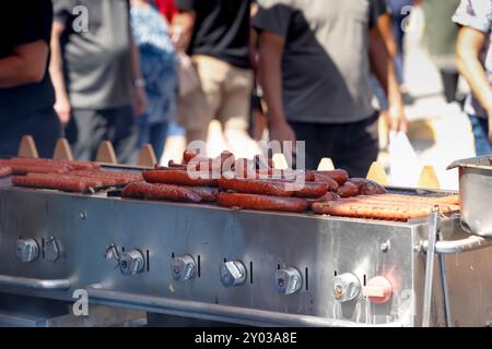 Una vista di cuccioli di hot dog e salsicce grigliate su un grande barbecue, visto in un carnevale locale. Foto Stock