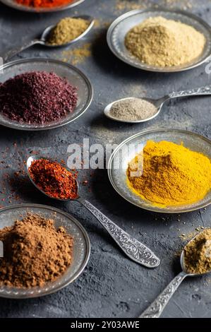 Assortimento di spezie naturali su cucchiai d'argento vintage o piatti su sfondo di pietra rustica scura, concetto di spezie salutari Foto Stock