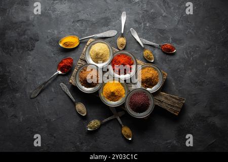 Assortimento di spezie naturali su cucchiai d'argento vintage o piatti su sfondo di pietra rustica scura, concetto di spezie salutari Foto Stock