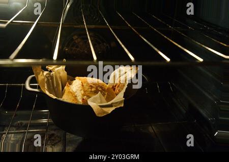 Vista dall'alto angolata di un pane nero olandese dorato con carta pergamena in un forno aperto con la luce accesa. Seduti all'interno della griglia del forno Foto Stock