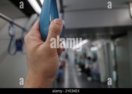 Immagine ravvicinata della mano di una persona che stringe una cinghia blu all'interno di un veicolo di trasporto pubblico, probabilmente un treno o una metropolitana. Foto Stock