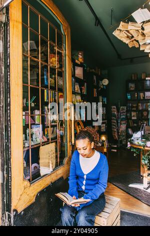 Una giovane donna che legge un libro seduto vicino alla porta della libreria Foto Stock