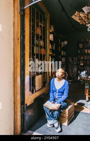 Giovane donna seduta alla luce del sole all'ingresso della libreria Foto Stock