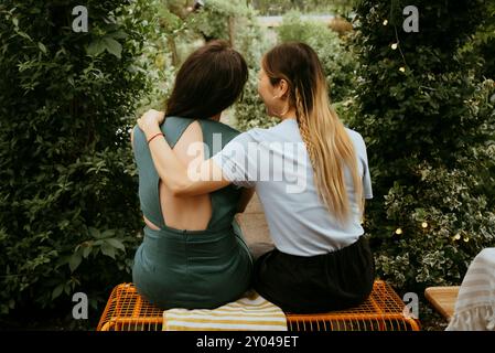 Vista posteriore delle amiche sedute sulla panchina vicino alle piante nel cortile posteriore Foto Stock