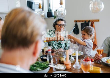 La nonna brinda con la nipote seduta a tavola durante la cena con la famiglia a casa Foto Stock
