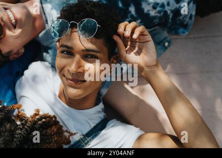 Ritratto di un giovane hipster con occhiali da sole e sdraiato a terra con gli amici alla luce del sole Foto Stock