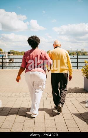Vista posteriore di un'infermiera che cammina con un anziano sul molo contro il cielo nuvoloso Foto Stock