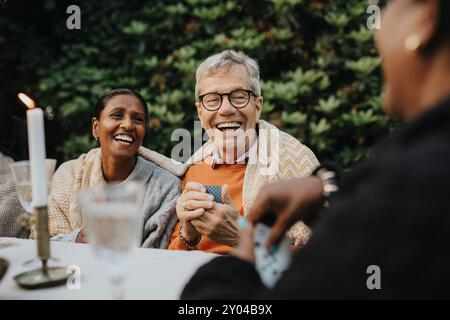 Allegro anziano che gioca a carte con i membri della famiglia alla festa in giardino Foto Stock