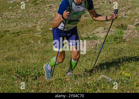 atleta con pali da trekking che scalano una significativa salita durante la maratona di montagna Foto Stock