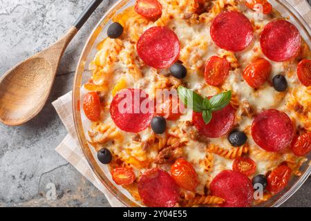 Casseruola per pizza con pasta tenera, carne di manzo dorata, salame, olive, peperoni e formaggio soffocati in salsa marinara, primo piano su in una ciotola di vetro Foto Stock