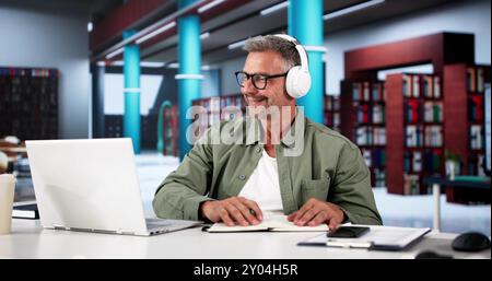 Happy Man studia su un computer portatile nella biblioteca Foto Stock