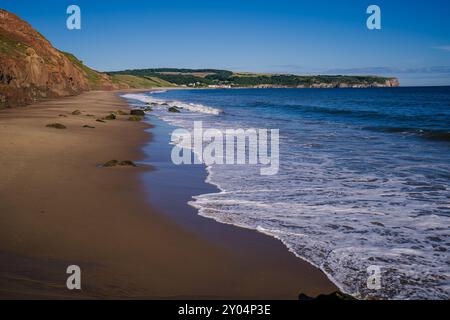 Guardando a nord lungo la spiaggia di Whitby's Upgang in una mattinata di sole con Sandsend in lontananza Foto Stock