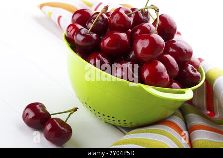 Ciliegie dolci mature in un colino verde su sfondo bianco Foto Stock