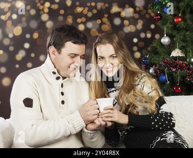 Ritratto di una felice coppia giovane sulle luci sfocate sullo sfondo vicino all'albero di Natale Foto Stock