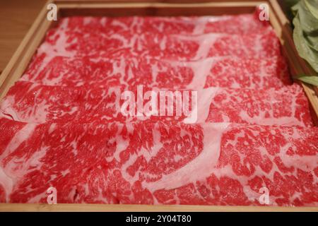 Un'immagine ravvicinata che mostra il manzo Wagyu marmorizzato a fette sottili sistemato ordinatamente in un vassoio di legno Foto Stock