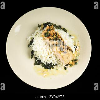 Delizioso pezzo di salmone su un letto di riso a grani lunghi, e spinaci, su un piatto verso il nero Foto Stock