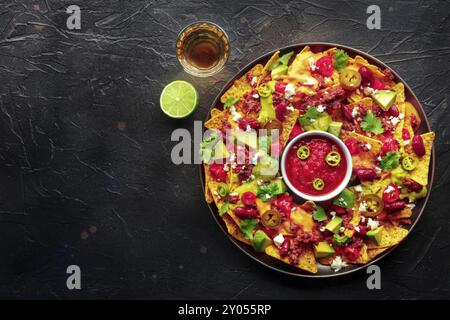 Nachos carichi. Patatine nacho messicane con manzo, shot piatto con salsa guacamole, salsa al formaggio, bevanda tequila, lime, con un posto per il testo Foto Stock