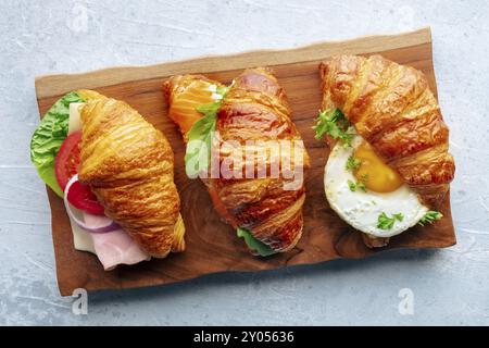 Varietà di panini con croissant. Vari croissant ripieni, piatti sospesi su una tavola di legno. Panini ripieni di prosciutto, salmone, uova, ecc. Foto Stock