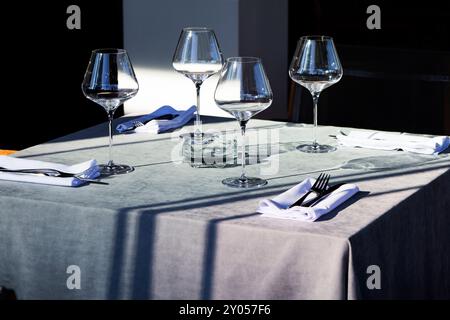 Sul tavolo, ci sono tre eleganti bicchieri da vino insieme a varie argenterie accuratamente disposte intorno a loro, creando un ambiente incantevole Foto Stock