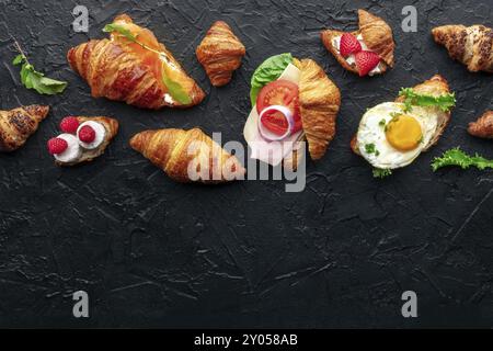 Assortimento di panini croissant. Vari croissant ripieni, piatti sospesi su sfondo di ardesia nera. Panini ripieni di prosciutto, salmone, uova, ecc. Foto Stock