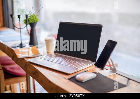 Spazio di lavoro accogliente: Computer portatile aperto, tazza di caffè, pianta e notebook su un tavolo di legno. La combinazione di elementi digitali e analogici crea una confortevole a Foto Stock