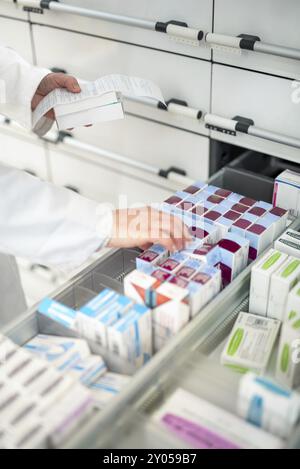 Una persona dispensa farmaci soggetti a prescrizione da un cassetto nel magazzino, evidenziando l'organizzazione e l'efficienza nella farmacia Foto Stock