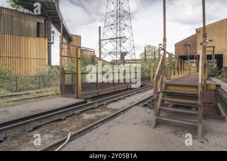 Sito industriale abbandonato con scale di metallo, vecchi binari ferroviari e circondato da alberi sotto un cielo nuvoloso, acciaierie HF4, Lost Place, Dampremy, Char Foto Stock