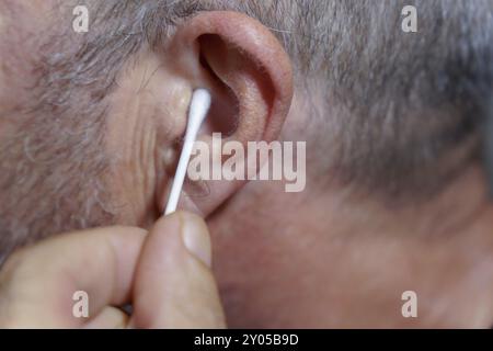 Primo piano di un uomo che pulisce le orecchie con un bastoncino di cotone Foto Stock