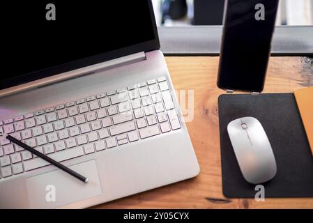 In una scrivania ordinata, un elegante notebook con schermo vibrante occupa un posto centrale, accompagnato da un mouse moderno e da uno smartphone elegante. Il pettine Foto Stock